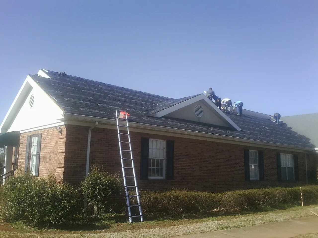 Crew tearing shingles off a brick ranch roof with a ladder set — Emergency Roof Repair work by our crew in Apollo