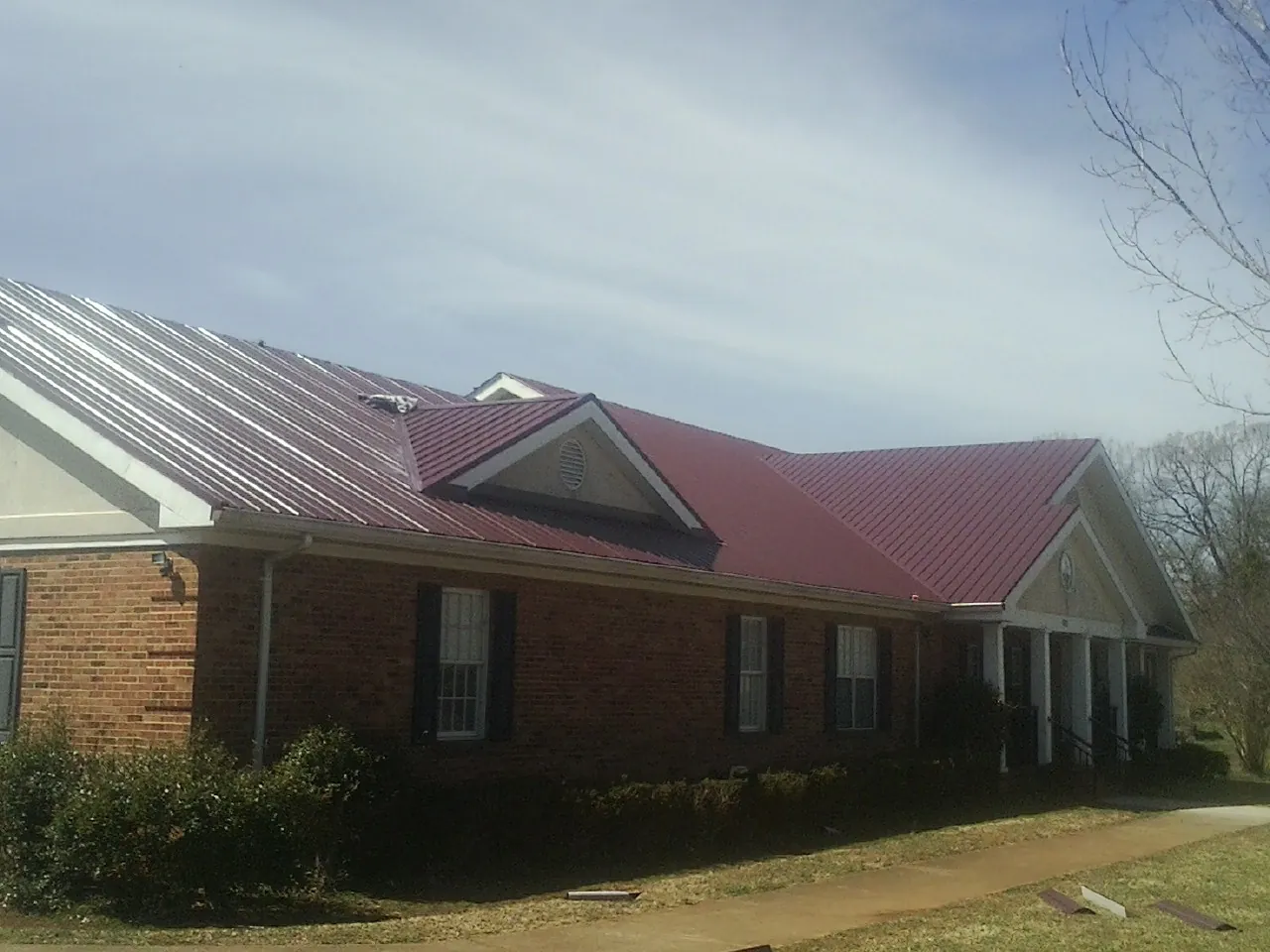 Red metal roof with gabled entries on a long brick building, from a Hail Damage Roof Repair job in Apollo