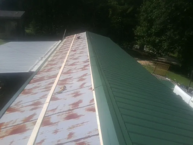 Old rusted panels beside newly installed green metal roofing — Wind Damage Roof Repair by Roofing Brothers in Apollo