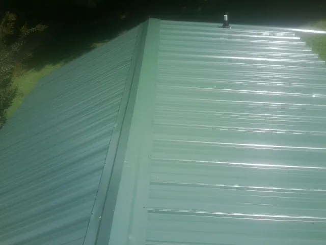 New green metal panels meeting at the ridge of a roof — Flat Roof Repair work by our crew in Apollo
