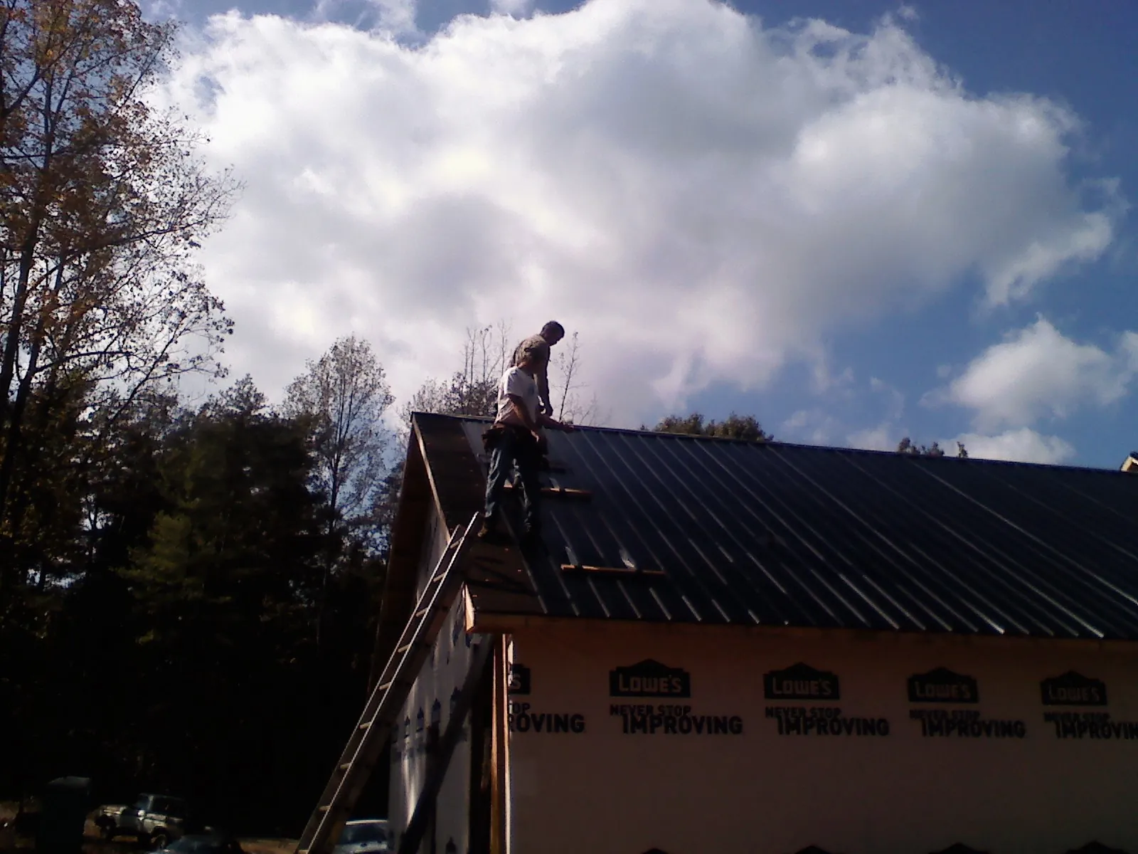 Roofer fastening dark metal panels high against a cloudy sky, from a Roof Inspection job in Apollo