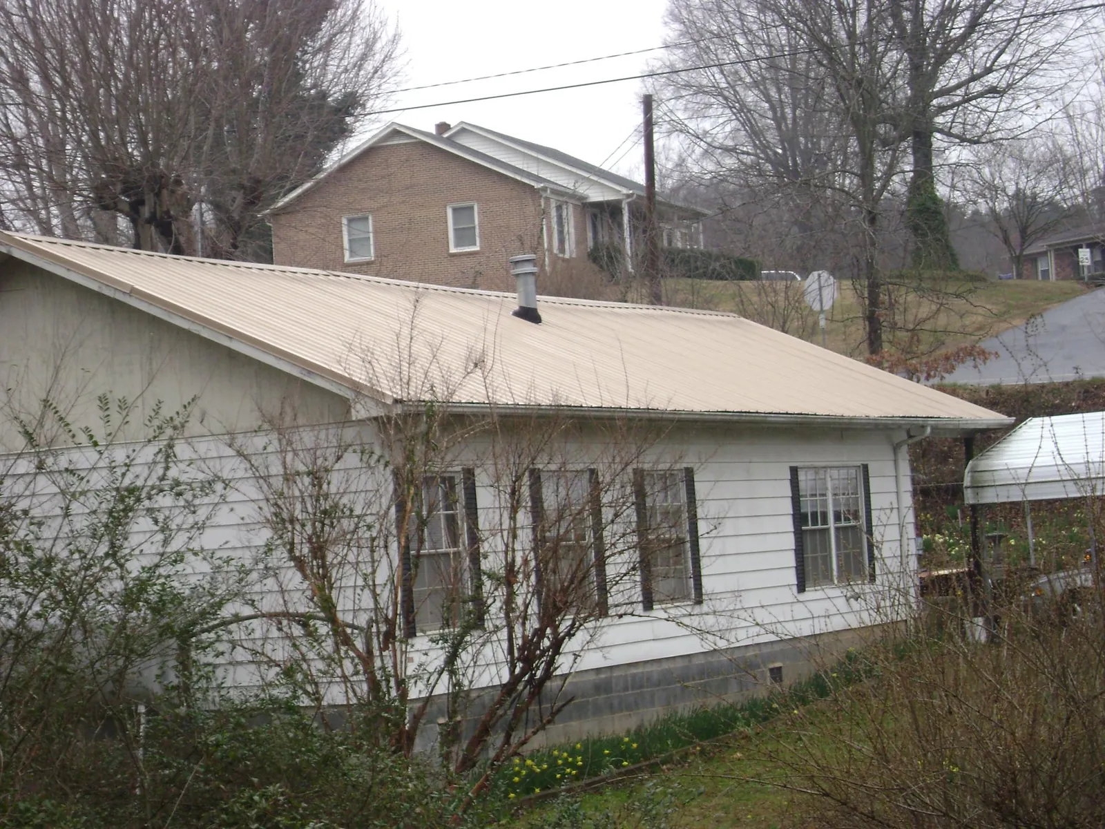 Tan metal roof on a white sided house set into a hillside — Commercial Roofing by Roofing Brothers in Apollo