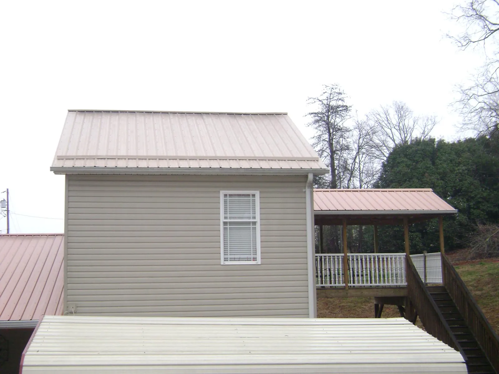 Tan metal roofs on a two story addition and attached porch, from a Roof Replacement job in Apollo